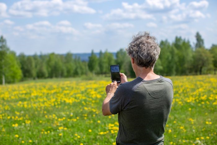 En person tar foto på ett fält utomhus med en mobiltelefon. Personen använder appen Geofoto.