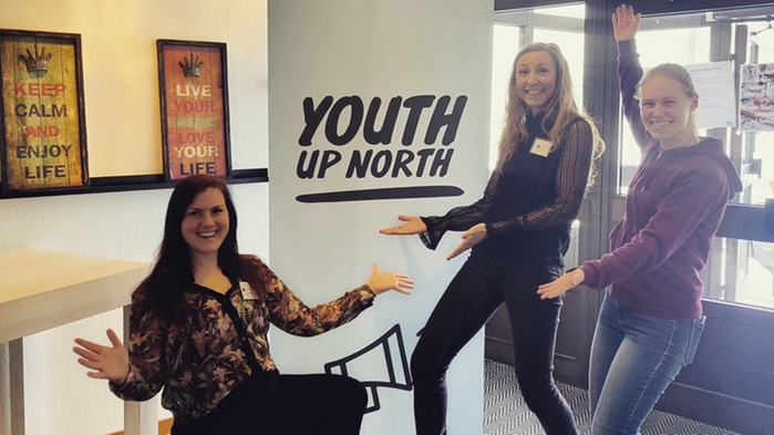 Tre glada tjejer framför en roll-up med texten "Youth Up North".