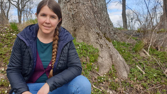 Ylva Berry är projektledare och arbetar med att främja miljömålet Ett rikt odlingslandskap på Länsstyrelsen i Stockholm. Hon sitter på huk i skogen med en blå täckjacka på sig. 