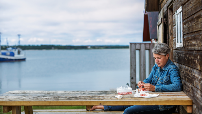 Kvinna vid ett bord. I bakgrunden syns en sjö eller ett hav.