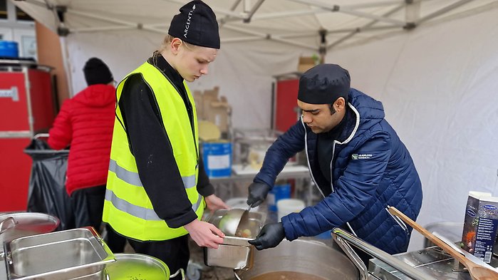 Två personer i ett tält där det serveras mat i samband med en beredskapsövning utomhus. 