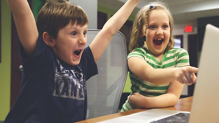 Två glada barn framför en dator.